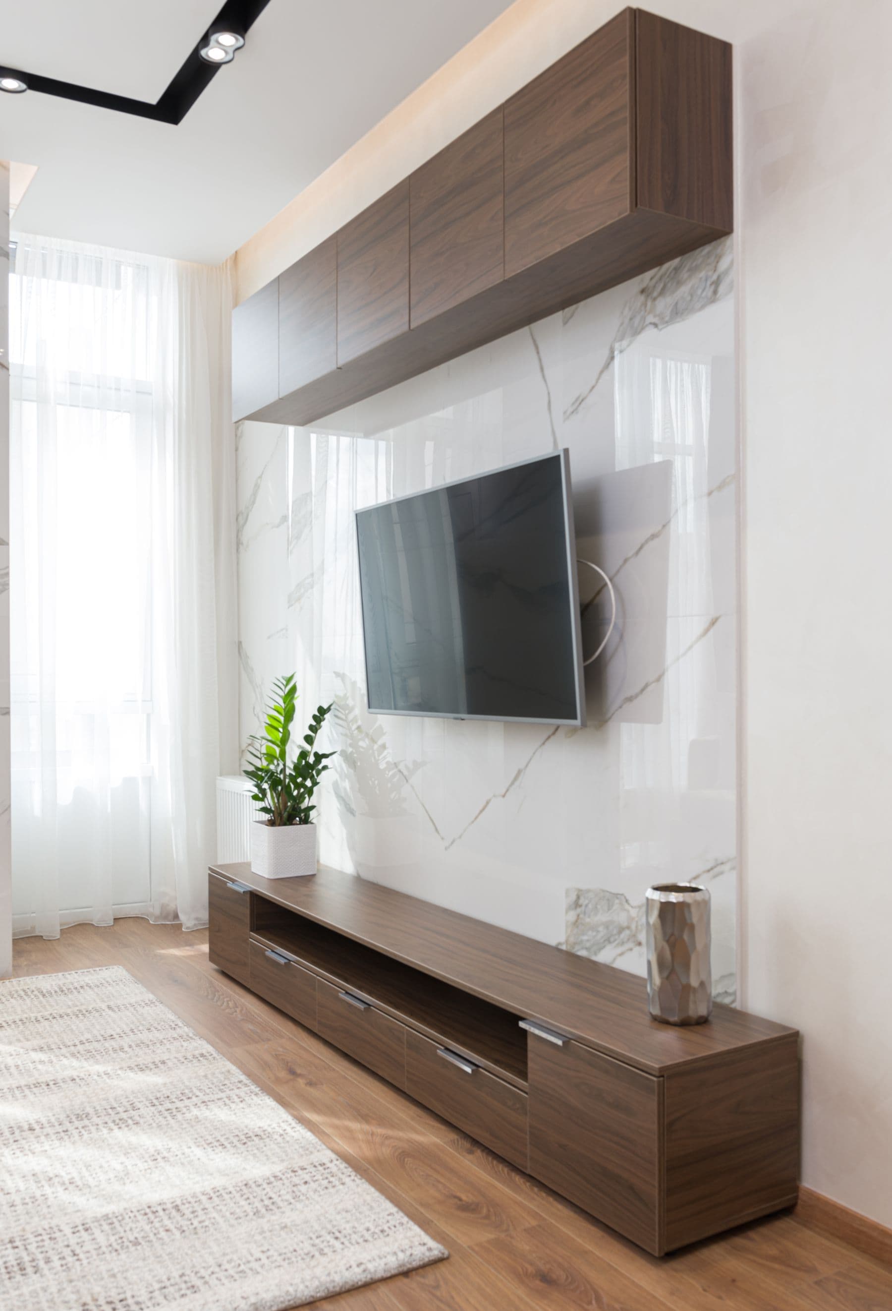 TV on a full-motion swivel mount over a marble-tile media wall with walnut cabinetry