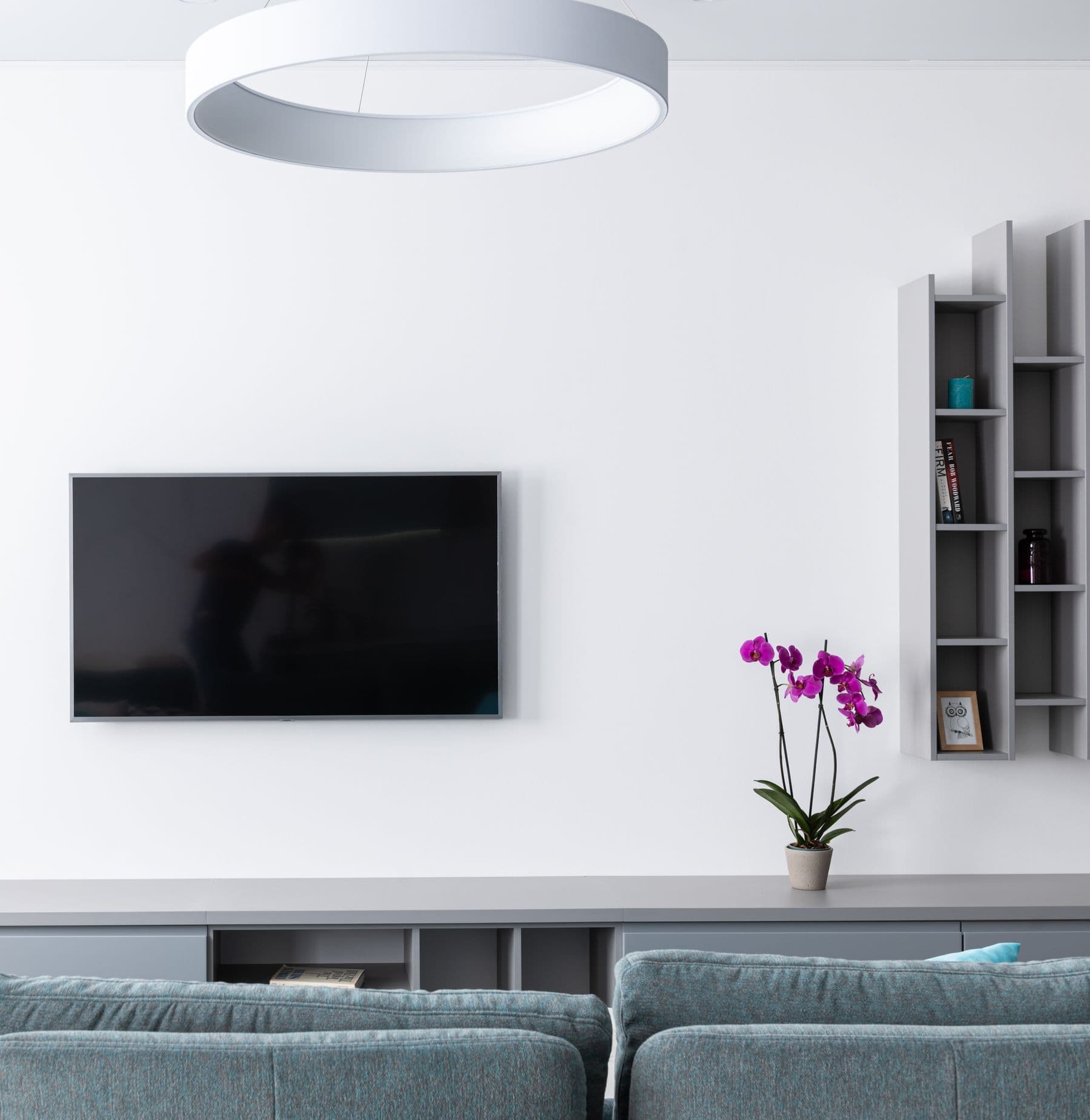 TV mounted on a bright white wall beside modular gray shelving over a long built-in media cabinet